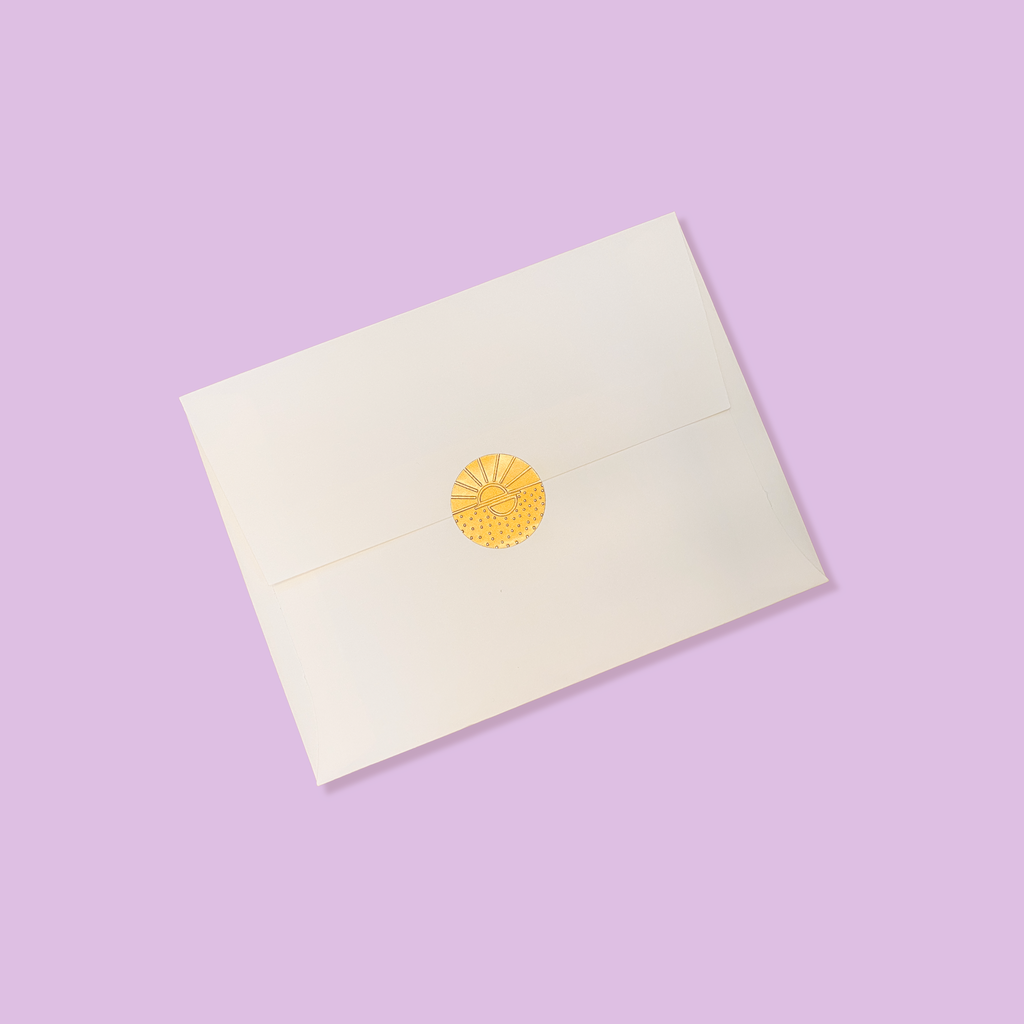 Creme colored envelope sealed with a golden vamarea sticker on a lilac colored background.