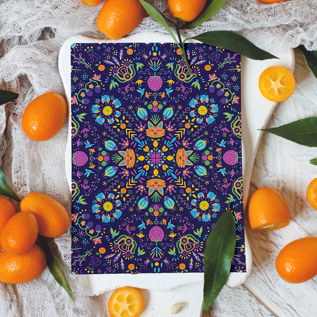 Fruit and nature themed portrait style greeting card with a pattern that repeats radially on a rich purple background. The design features bright orange foxes, bright blue flowers, purple strawberries, and yellow lemons among other graphics. The card is displayed on a white background with cumquats decorating the space around it. 