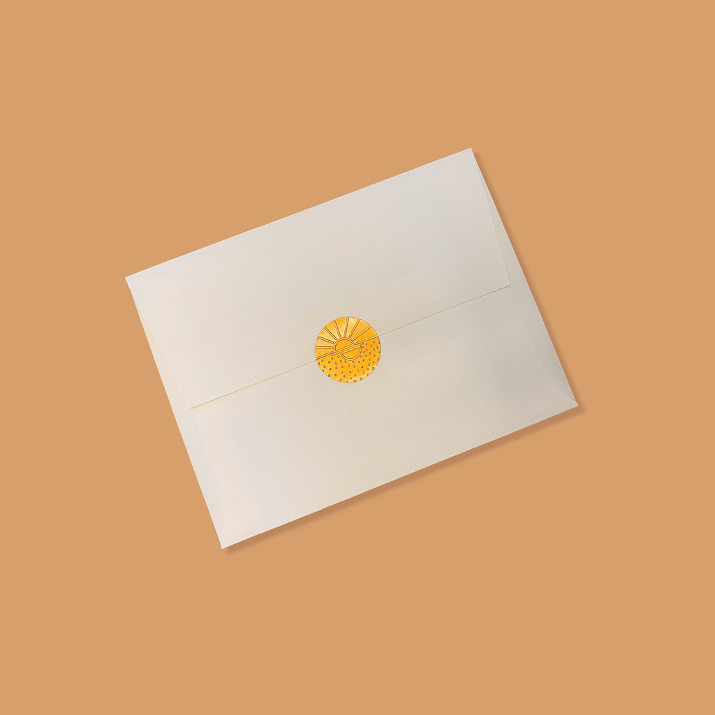 Creme colored envelope sealed with a golden vamarea sticker on a copper colored background.