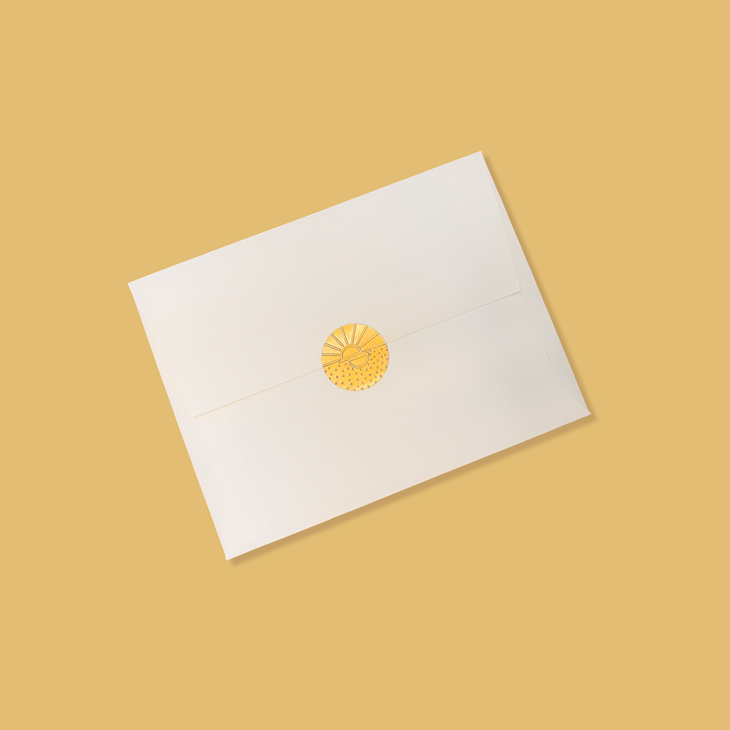 Creme colored envelope sealed with a golden vamarea sticker on a matte gold colored background.