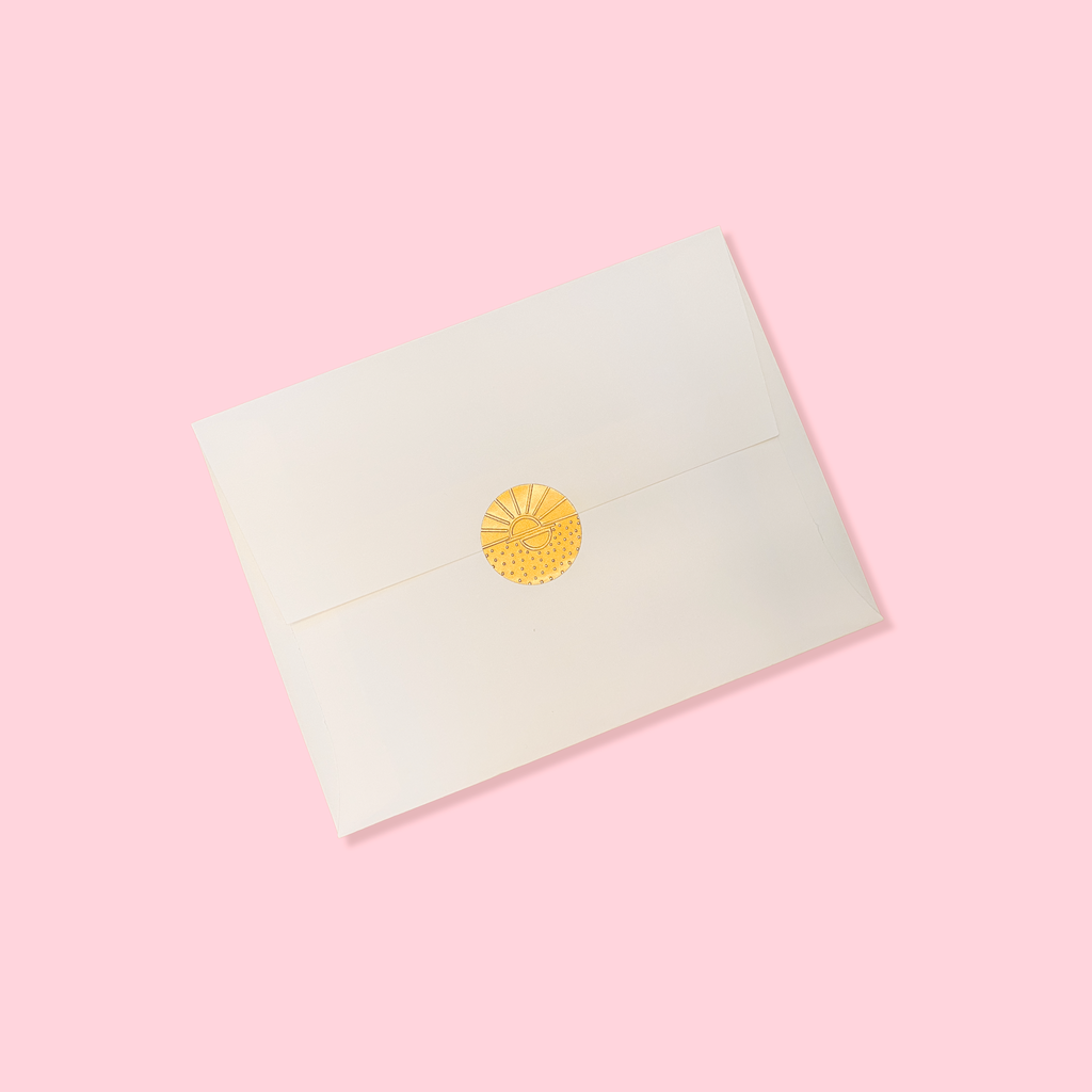 Creme colored envelope sealed with a golden vamarea sticker on a light pink colored background.