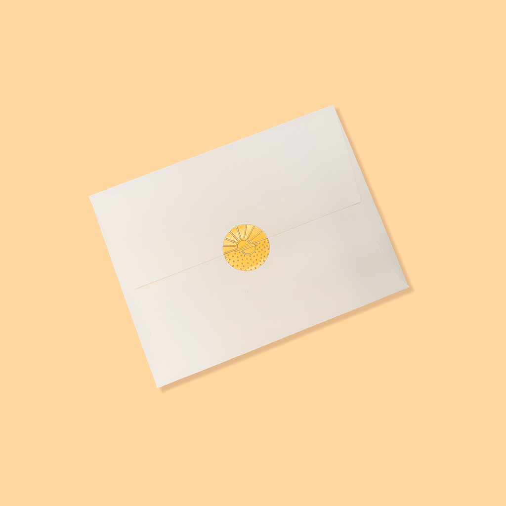 Creme colored envelope sealed with a golden vamarea sticker on a yellow-orange colored background.