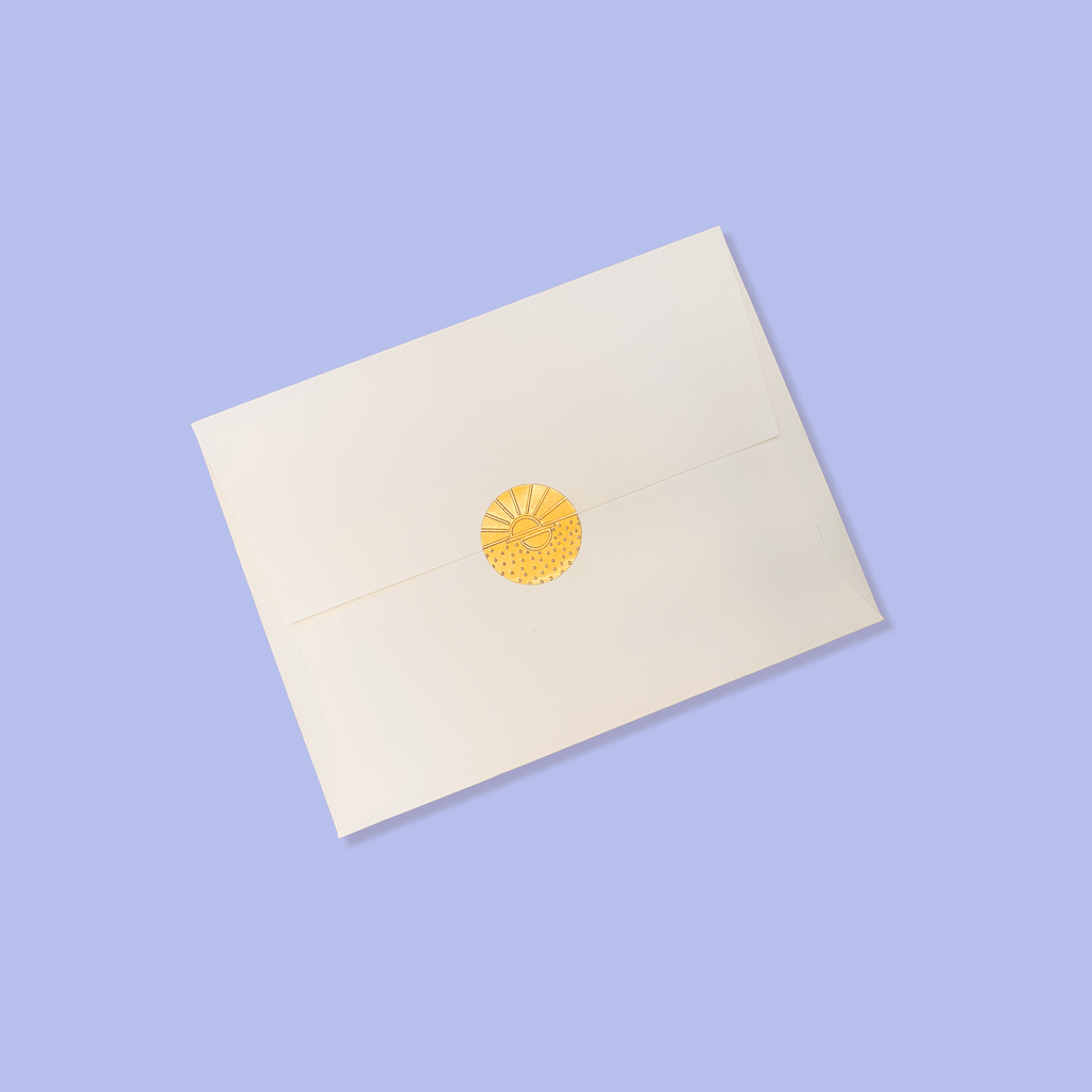 Creme colored envelope sealed with a golden vamarea sticker on a light purple colored background.