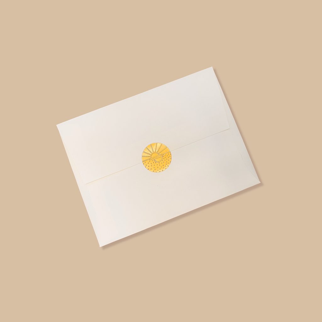 Creme colored envelope sealed with a golden vamarea sticker on a sandy brown colored background.
