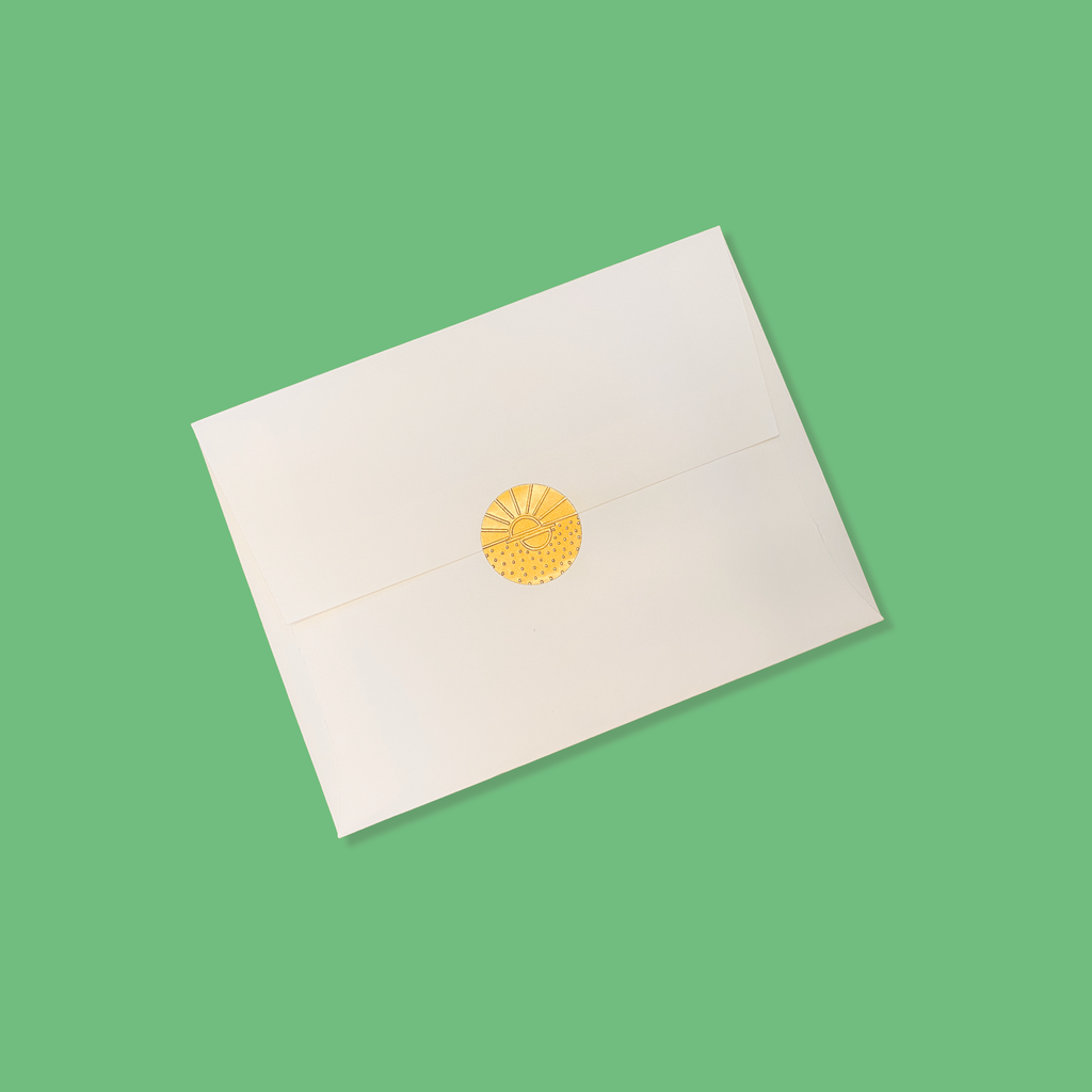 Creme colored envelope sealed with a golden vamarea sticker on a green colored background.