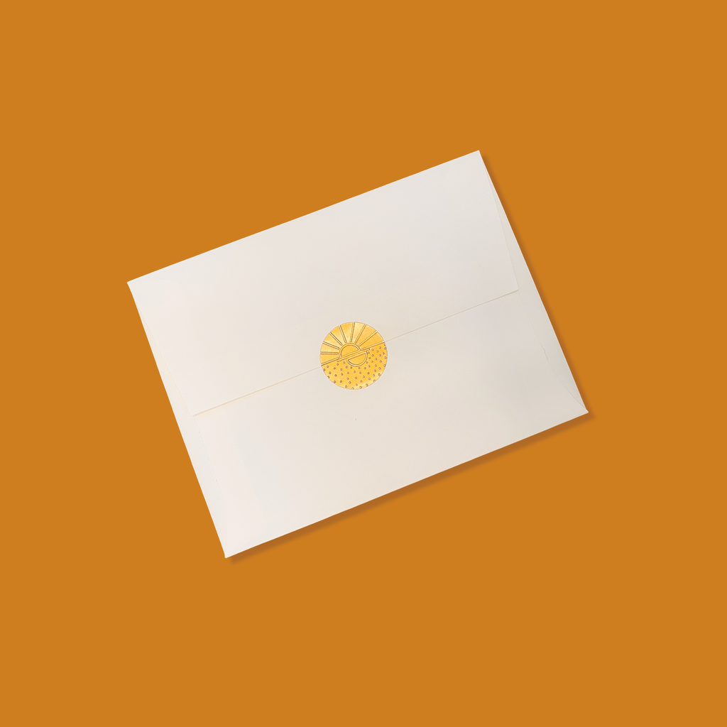 Creme colored envelope sealed with a golden vamarea sticker on an orange colored background.