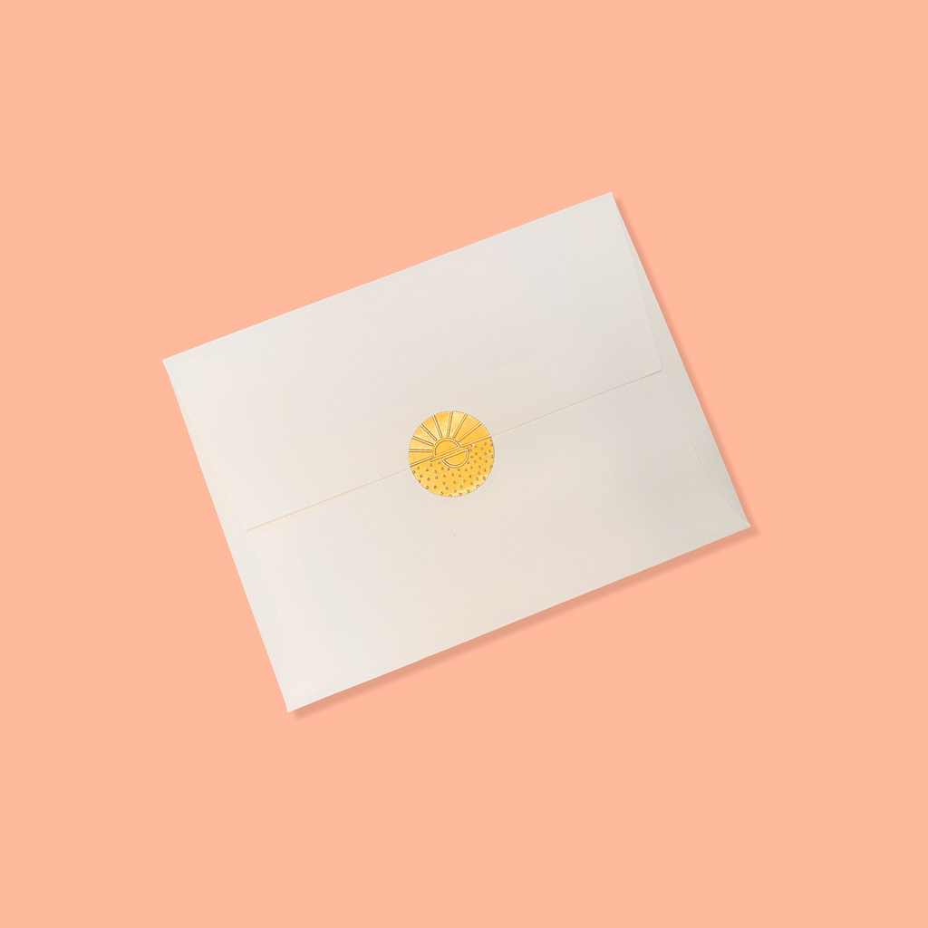 Creme colored envelope sealed with a golden vamarea sticker on a peach colored background.