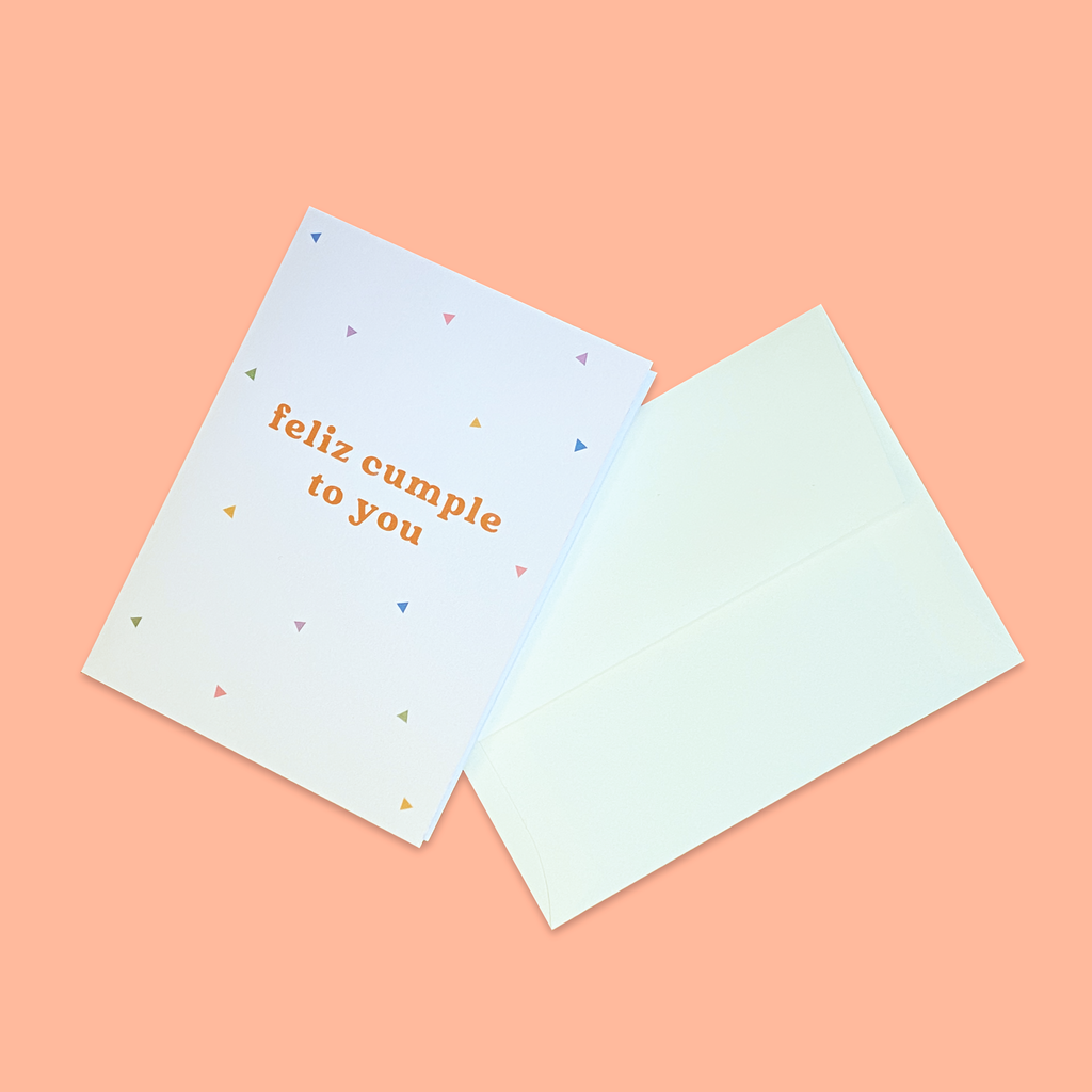"Feliz Cumple To You" greeting card next to creme colored envelope.