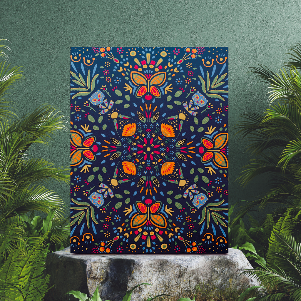 Portrait style greeting card featuring elements endemic and traditional to Mexico with a pattern that repeats radially on a rich blue background. The design features a bright blue jaguar, corn, chiles, nopales, and even a quetzal among other graphics. The card is displayed upright on a grey stone with palm fronds around it.